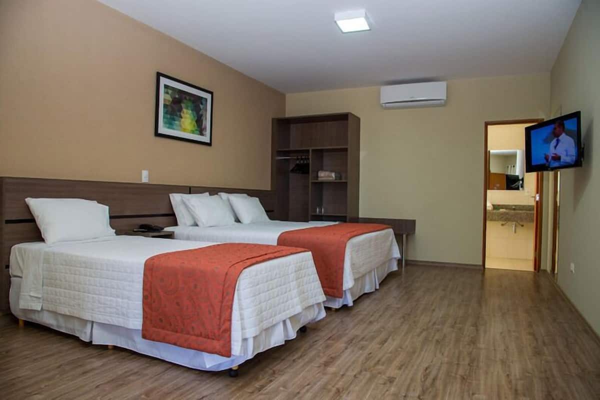 Une chambre d’hôtel avec deux lits, une télévision, une armoire et un tableau au mur.