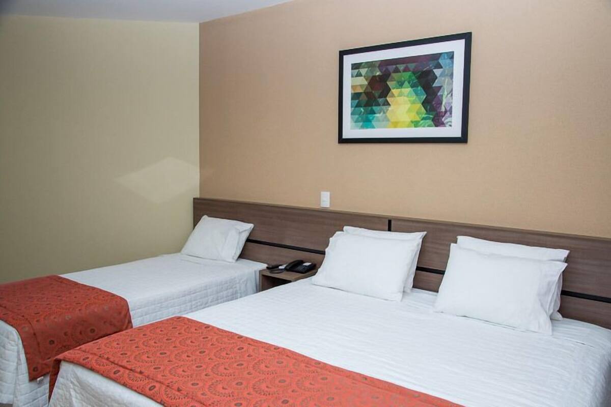 Une chambre d’hôtel avec deux lits, une œuvre d’art encadrée au mur et un téléphone sur la table de chevet.