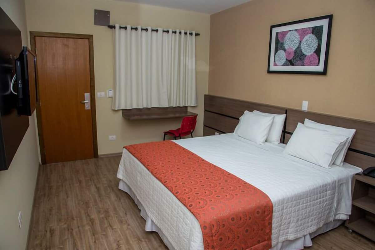 Une chambre d’hôtel avec un lit, une chaise rouge, une porte et un tableau encadré au mur.
