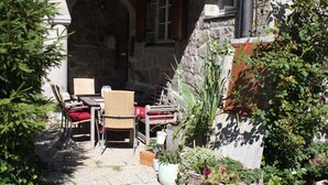 Une terrasse extérieure avec une table et des chaises, entourée de plantes en pot et d’un mur de pierre.