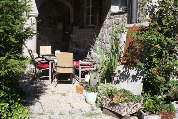 An outdoor patio with a table and chairs, surrounded by potted plants and a stone wall.