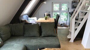 Un salon chaleureux de style industriel, avec un canapé d’angle vert, une table basse en bois et un escalier menant à un niveau supérieur.