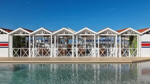 A row of white, open-air structures with red roofs, each with a wooden deck and seating area, overlooking a clear blue sky. - Augustus Lido (Forte dei Marmi)