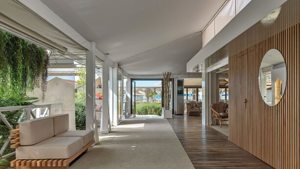 A modern interior with a sofa, wooden flooring, and a view of greenery outside. - Augustus Lido (Forte dei Marmi)