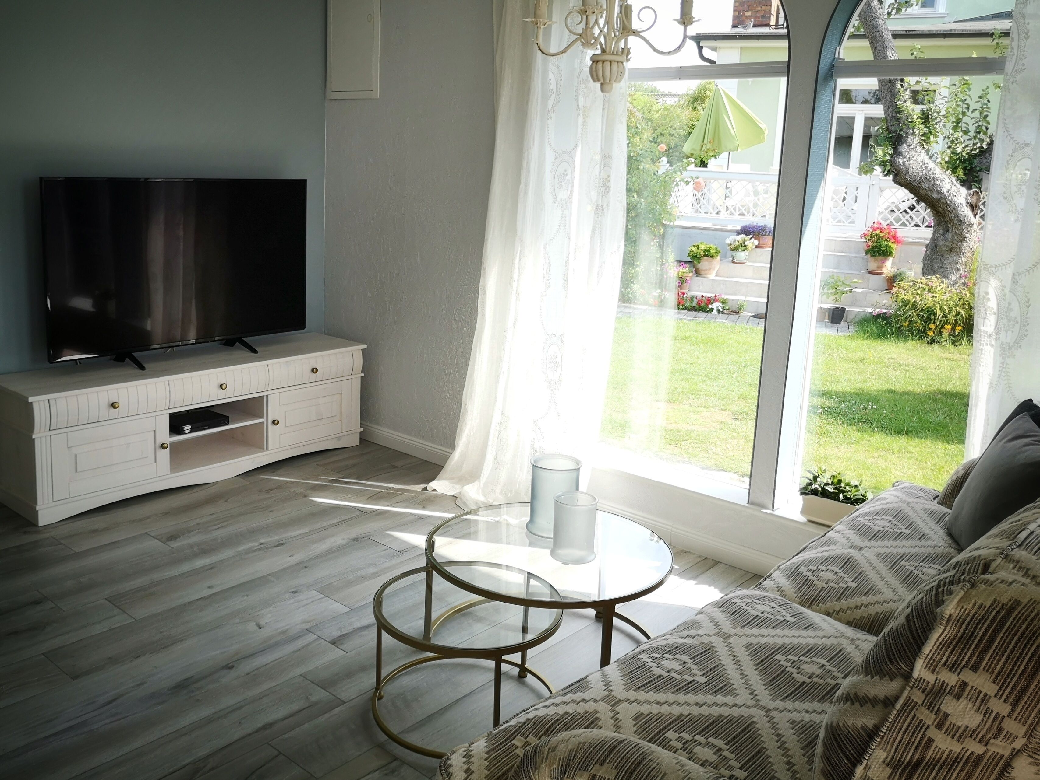 Un salon doté d’un téléviseur à écran plat, d’un meuble de rangement blanc en bois, d’une table basse ronde en verre et d’un canapé à motifs.