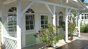 A covered porch with white railings and green siding, featuring multiple windows and potted plants.