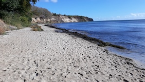 A sandy beach with a rocky cliff and a clear blue sky.