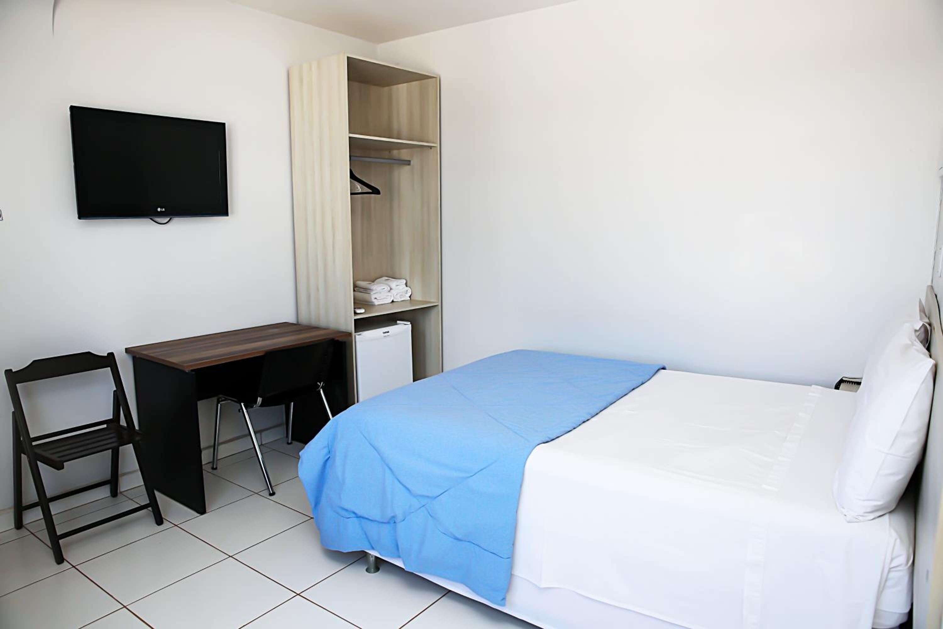 A bedroom with a bed, a desk, a chair, a TV, and a wardrobe.