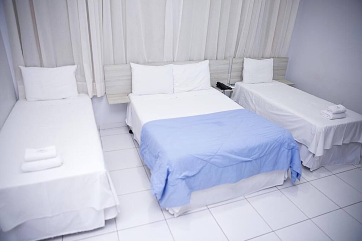 Ett hotellrum med tre sängar, vita sängkläder och ett klinkergolv.