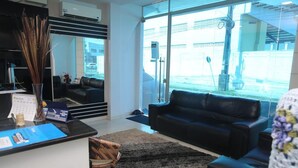 A modern hotel lobby with a reception desk, a black leather sofa, a wicker chair, and a large window offering a view of the outside. - Bellonorte Hotel (Altamira)