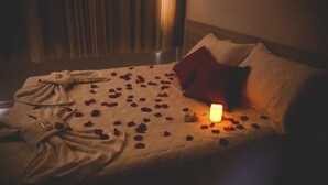 A bed with rose petals scattered on it, a lit candle, and a robe on the floor. - Bellonorte Hotel (Altamira)