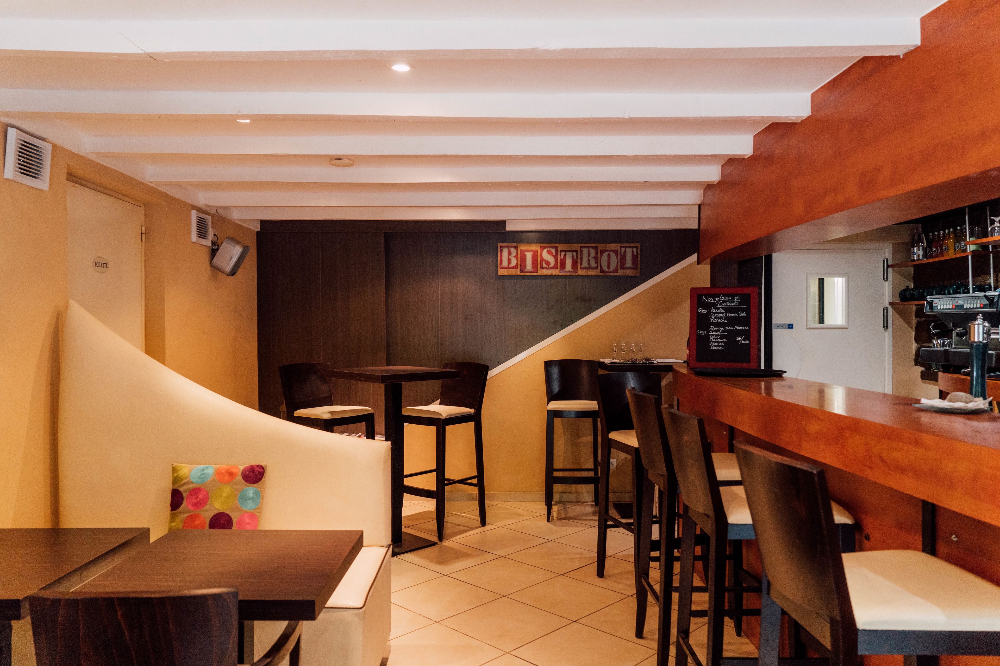 A restaurant interior with a bar area, wooden tables, and chairs.