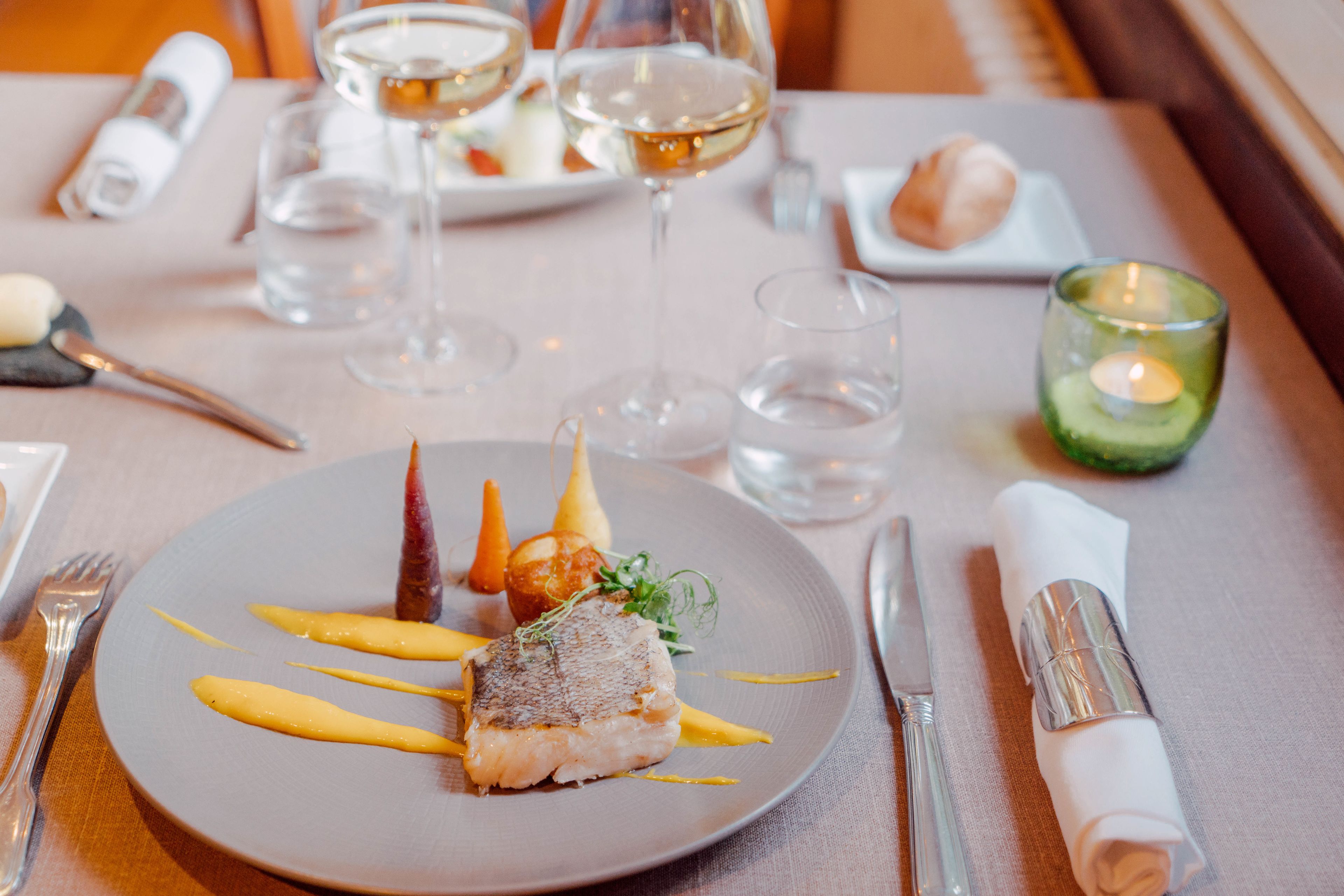 A dining table set with a plate of food, glasses, and a candle.