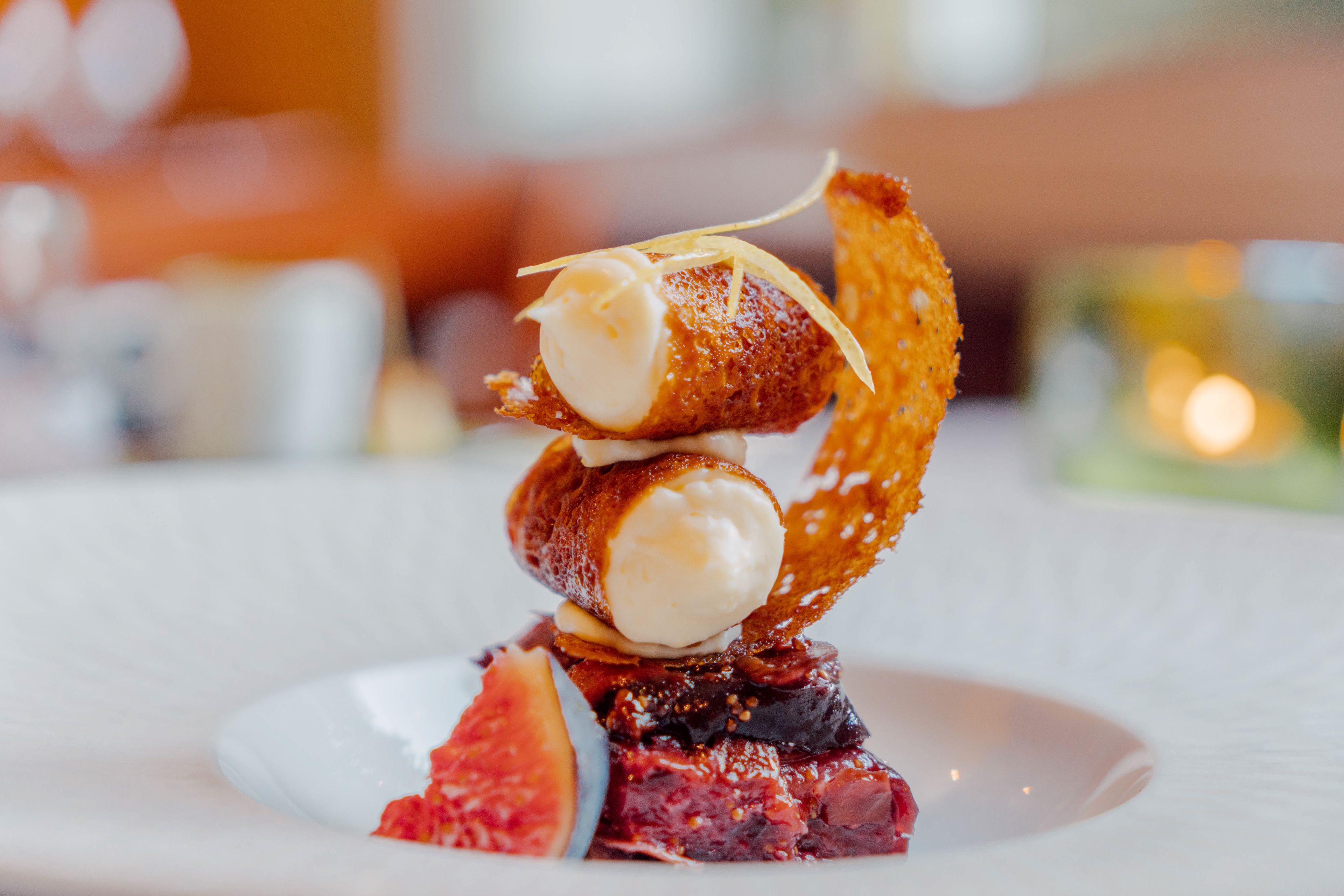Ein Dessert mit einer Kugel Eis auf einem Kuchenstück, dazu ein Obstscheibe und ein Waffel.