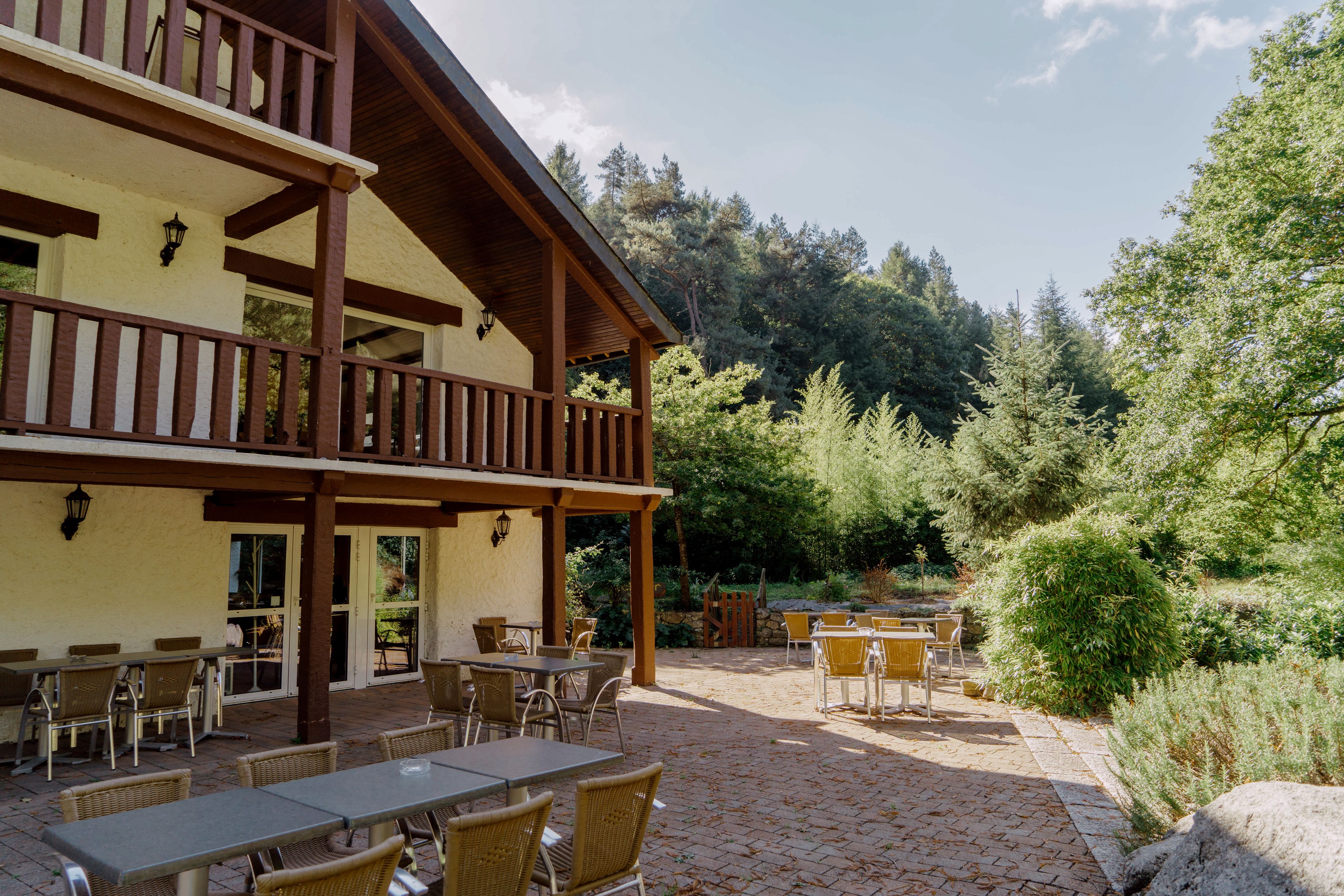 A building with a wooden balcony and outdoor seating area with tables and chairs.