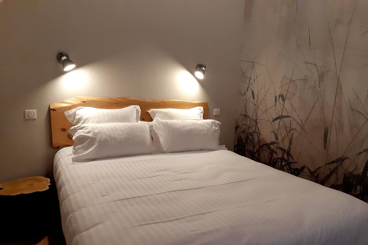 Un lit bien fait, avec du linge de lit blanc, une tête de lit en bois et deux lampes de lecture fixées au mur.