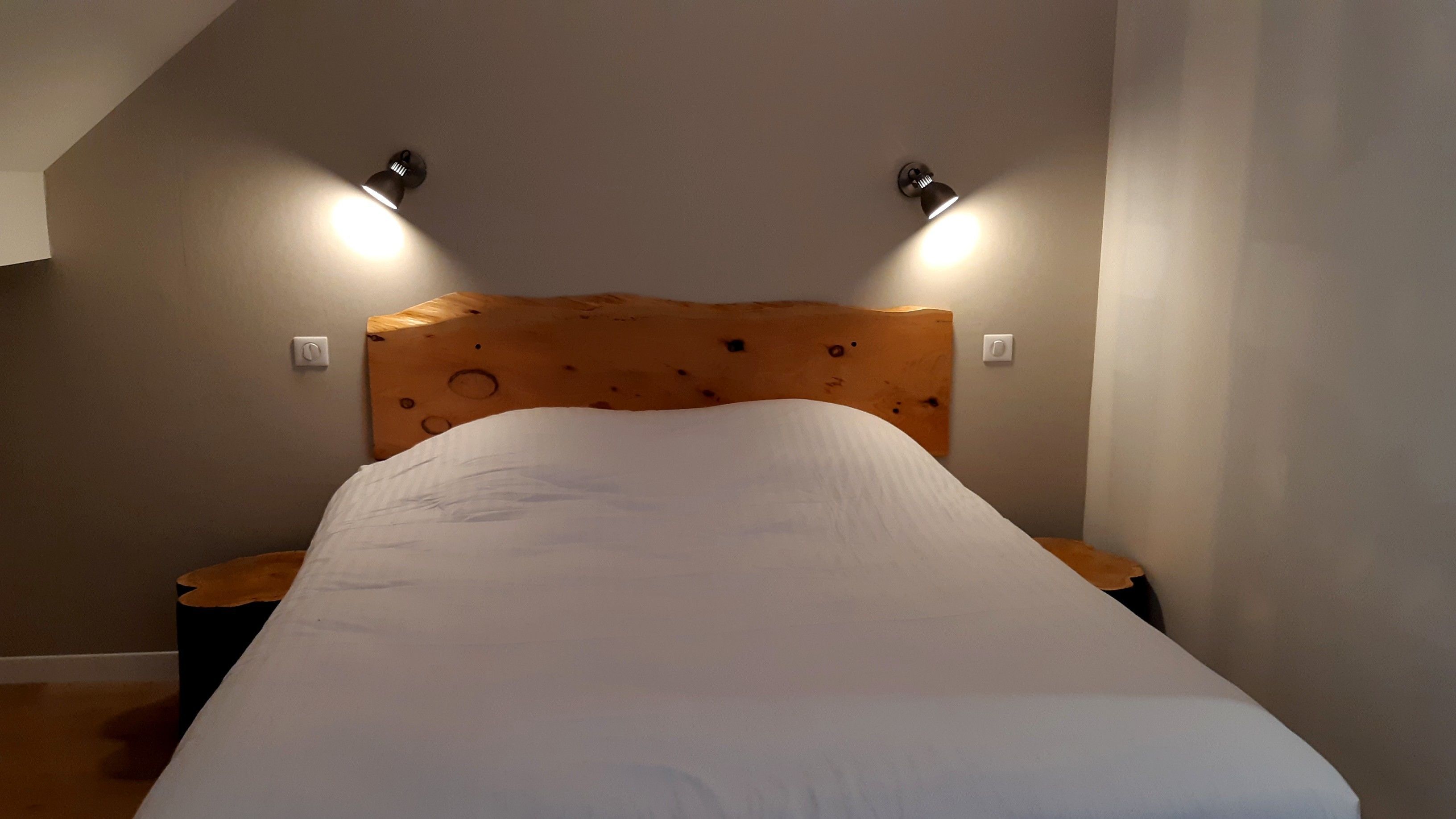 Een slaapkamer met een houten hoofdeinde, twee bedlampen en een witte spreidek.