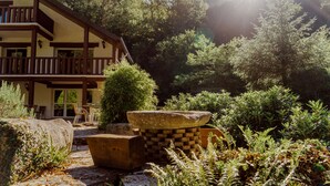 A lodge with a stone fireplace, outdoor seating, and a forested backdrop.