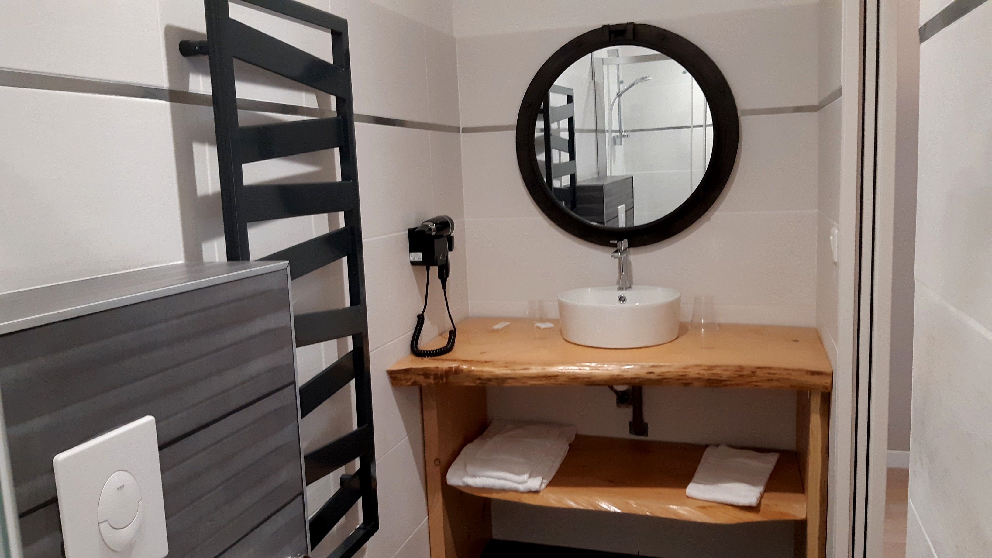 Een badkamer met een houten wastafelmeubel, een witte wasbak, een spiegel en een handdoekhouder.