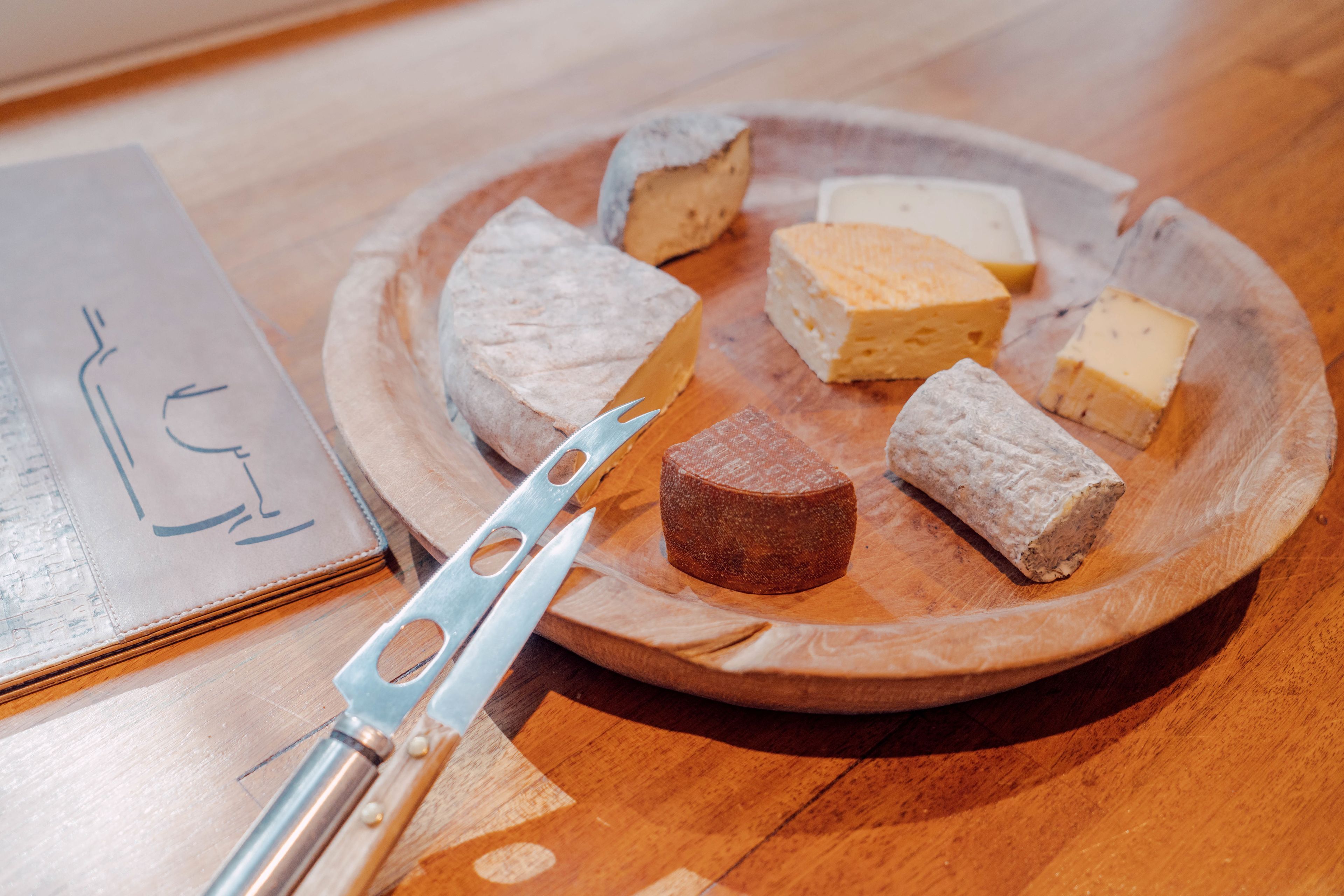 Een houten bord met verschillende kazen en een kaasmes op een houten tafel.