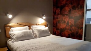 A neatly made bed with white linens and two wall-mounted lights above it.