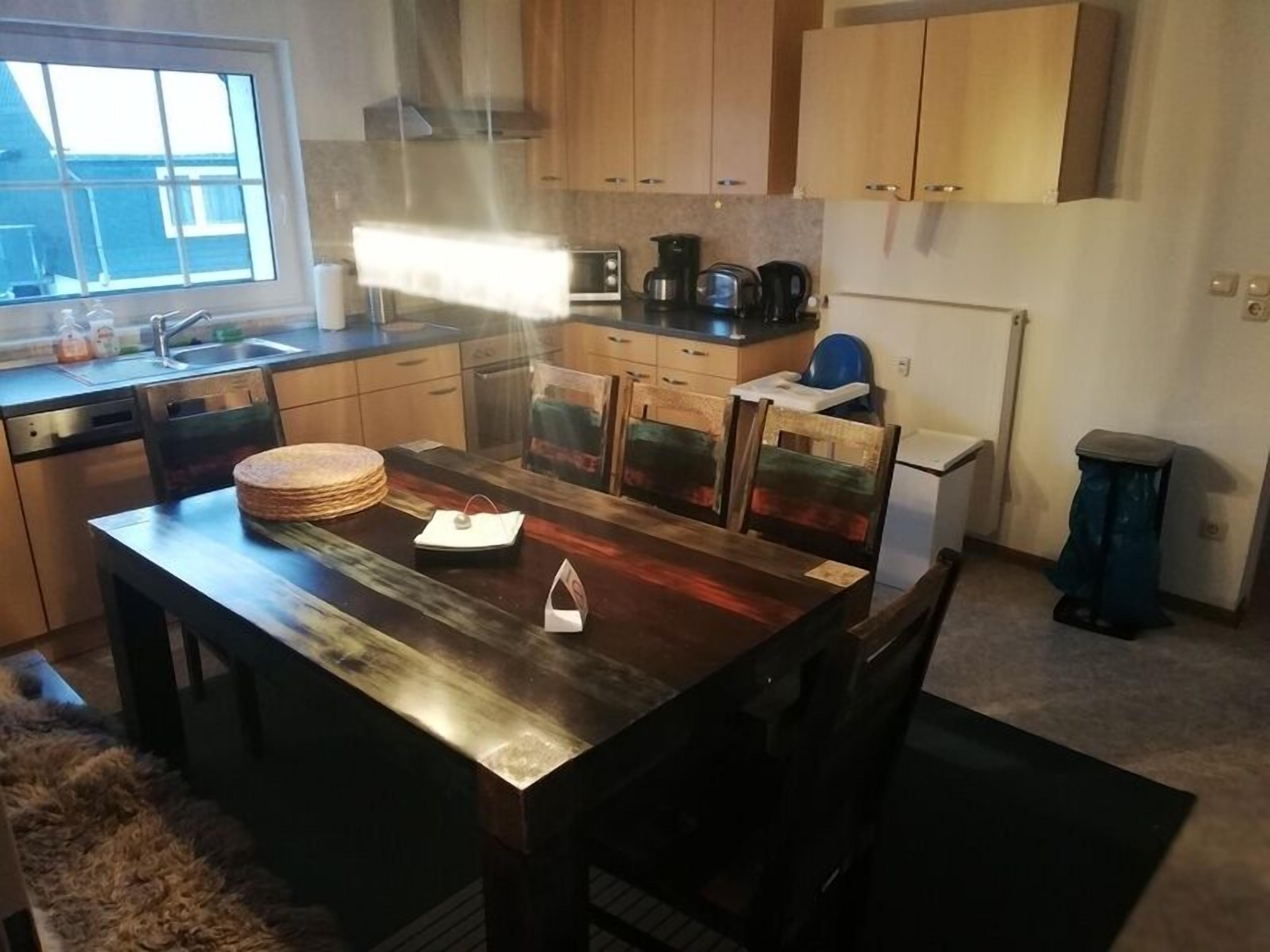 A modern kitchen with wooden cabinets, a stainless steel countertop, and a dining area with a wooden table and chairs.