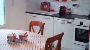 A compact kitchen with white cabinets, a small dining table with chairs, and a red kettle on the counter. - le Temps des Cerises (Vinsobres)