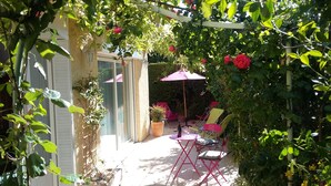 A garden patio with a table and chairs, a potted plant, and a pergola with a pink umbrella. - le Temps des Cerises (Vinsobres)
