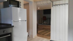 Cocina compacta con microondas, horno y refrigerador. Se ve un piso de madera y un pequeño comedor con una silla.