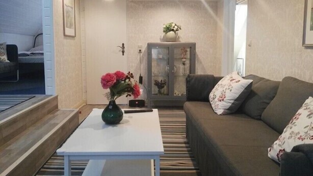 Una sala de estar con un sofá, una mesa de centro blanca, un aparador con puertas de cristal y una planta pequeña sobre la mesa.