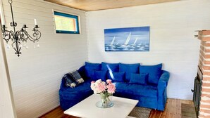 A living room with a blue sofa, a white coffee table, a painting of sailboats, a chandelier, and a fireplace. - Little Finland (Jyväskylä)