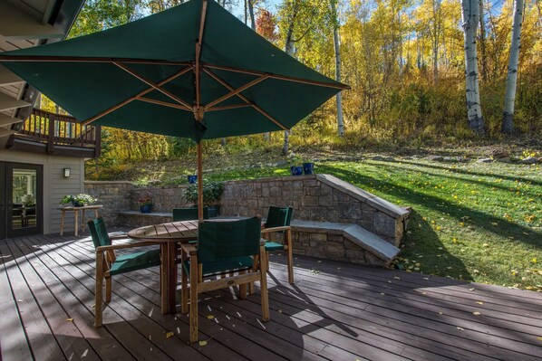 Une terrasse en bois avec une table et des chaises, un parasol vert et un mur en pierre.