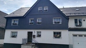 A two-story house with a dark blue roof, white walls, and a small front porch with a black railing. - Nijole Apartment (Winterberg)