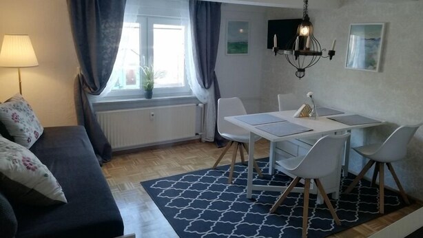 A modern living room with a sofa, dining table, chairs, and a chandelier. - Nijole Apartment (Winterberg)