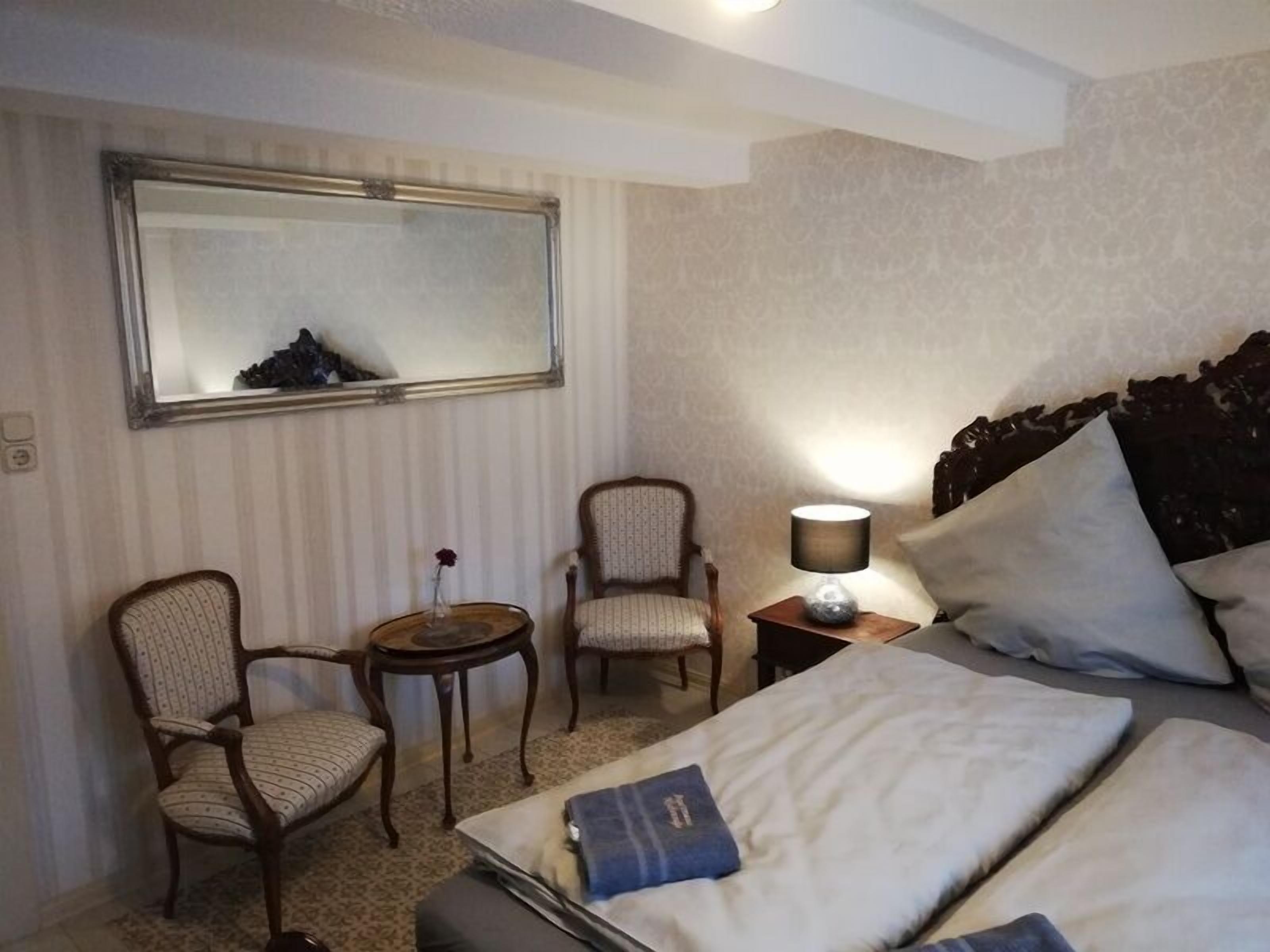 A hotel room with a bed, two chairs, a small table, a lamp, and a mirror on the wall.