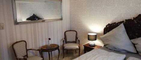 A hotel room with a bed, two chairs, a small table, a lamp, and a mirror on the wall.