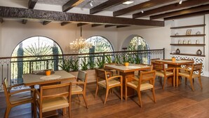 A dining area with wooden tables and chairs, large arched windows, and a chandelier. - Residencial Sênior Club Leger (São Paulo)