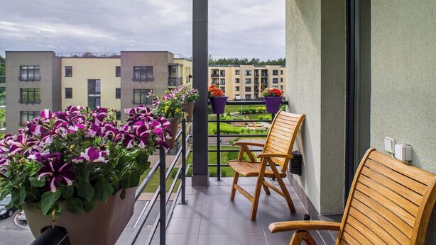 Ein Balkon mit einem Holzstuhl, Blumentöpfen und Blick auf andere Gebäude.