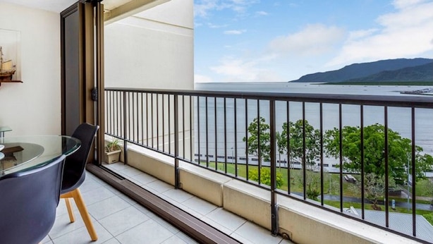 A balcony with a glass table and chairs, a view of a body of water, and a mountain in the distance. - Cairns Ocean View Apartment in Aquarius (Cairns)
