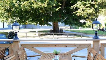 An outdoor seating area with wooden tables and chairs, a lamp post, and a large tree providing shade.