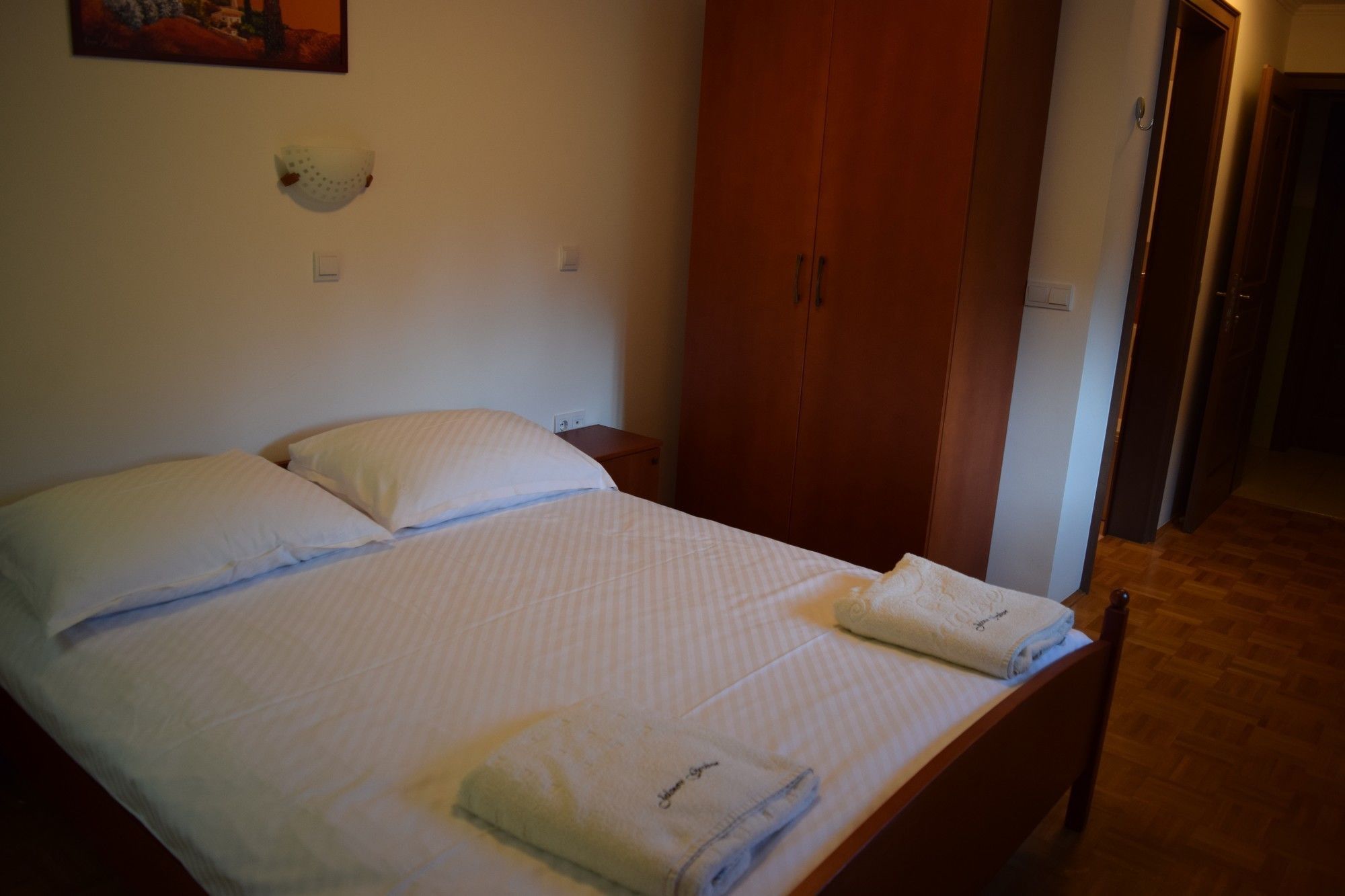 Ein ordentlich bezogenes Bett mit Kissen und gefalteten Handtüchern, ein Holzschrank und eine Wandleuchte.