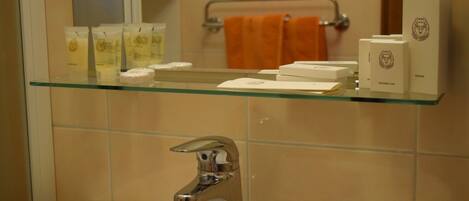 Ein Badezimmer mit einer Glasablage für Toilettenartikel, einem weißen Waschbecken mit chromfarbenem Wasserhahn und einem Handtuchhalter mit einem orangefarbenen Handtuch.
