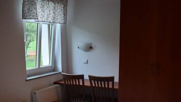 Een slaapkamer met een bed, twee stoelen, een tafel, een radiator en een raam met gordijnen.