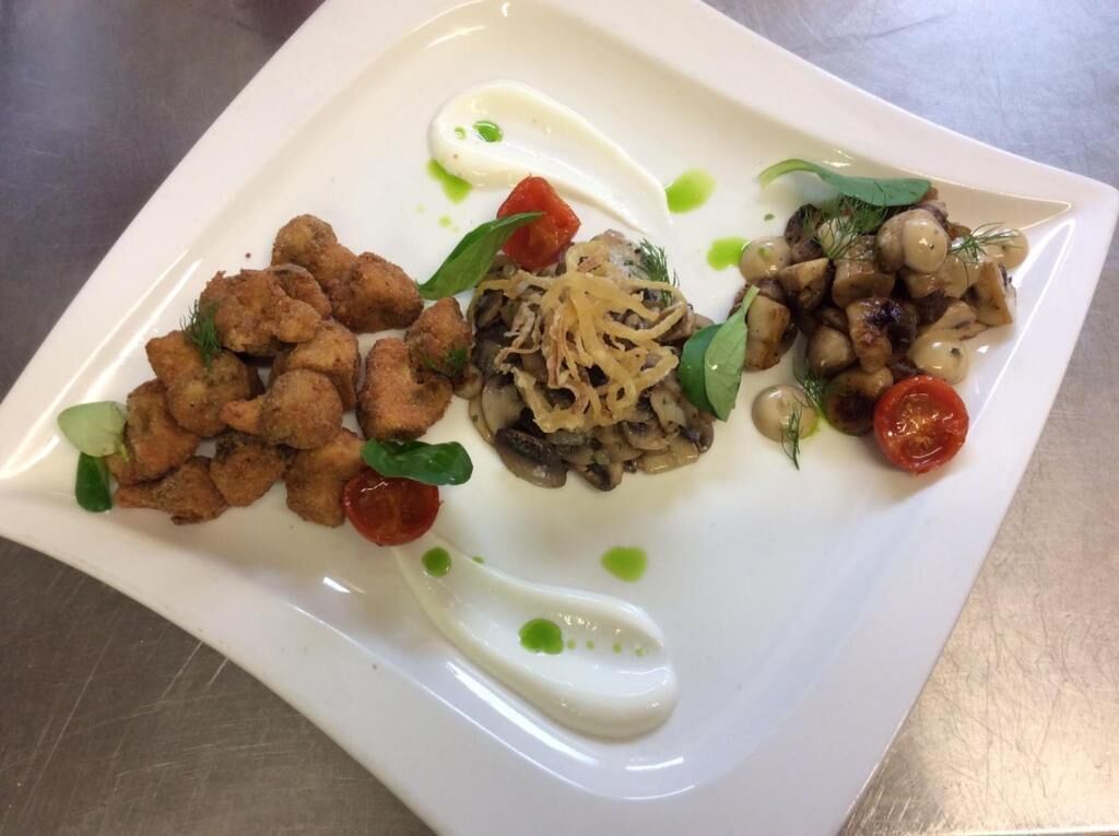 Un plato blanco con diversos alimentos, incluyendo trozos fritos, setas y guarniciones.