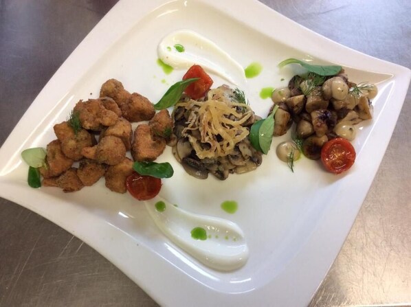 Un plato blanco con diversos alimentos, incluyendo trozos fritos, setas y guarniciones.