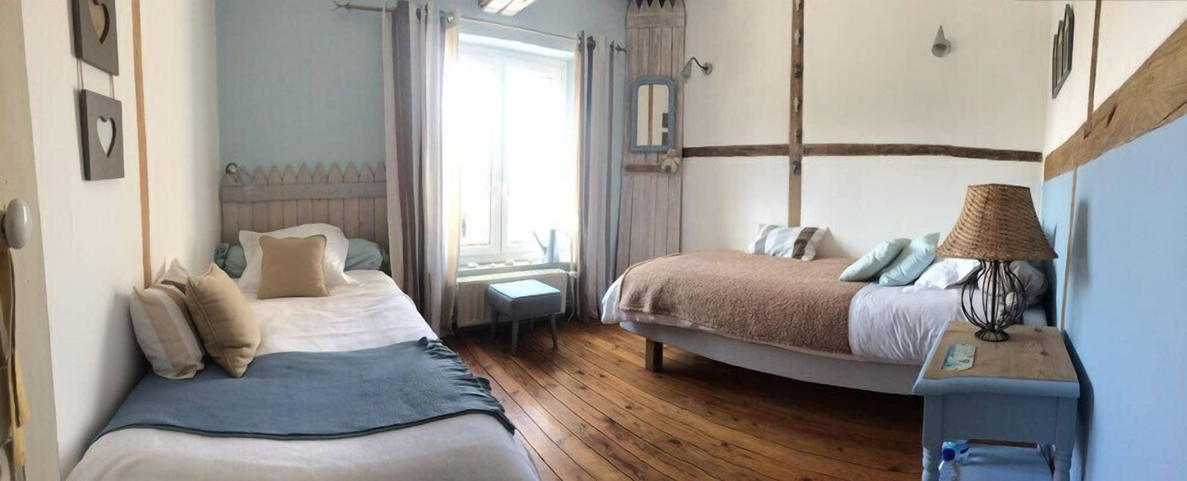 A bedroom with two beds, a small table, a lamp, and a window with curtains.