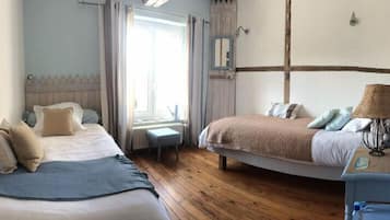 A bedroom with two beds, a small table, a lamp, and a window with curtains.
