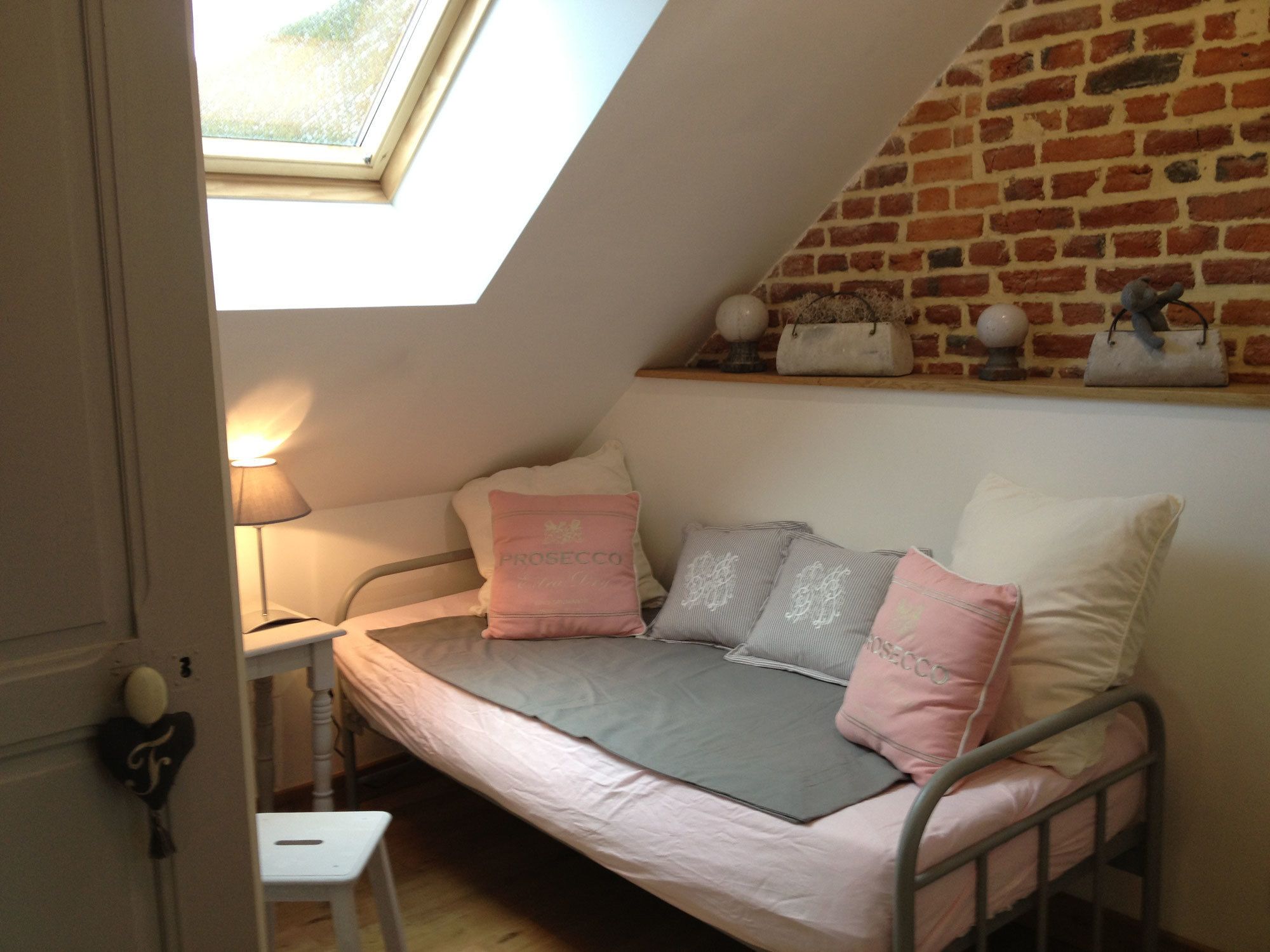 Un dormitorio estilo loft acogedor, con techo inclinado, tragaluz, cama con ropa de cama rosa y gris, y pared de ladrillo.