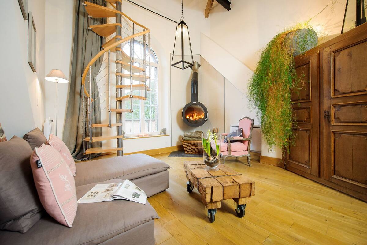 Ein gemütliches Wohnzimmer mit Wendeltreppe, Kaminofen und hängender Pflanze.