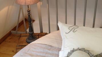 A neatly made bed with a white comforter and pillows, a metal headboard, and a floor lamp with a beige shade.
